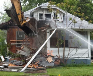 excavator demolishing a small white home