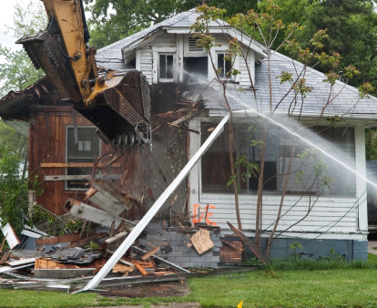 excavator demolishing a small white home